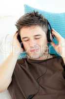 Attractive young man listening to music lying on a sofa