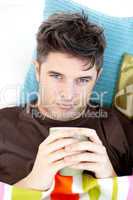Sick man lying on a sofa holding a cup