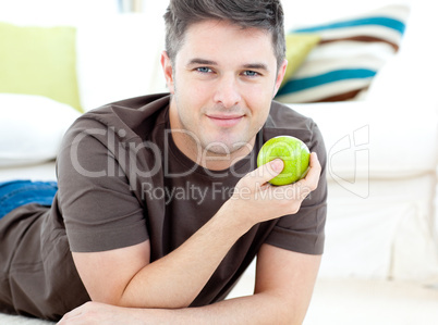 Positive man holding a green apple lying on the floor