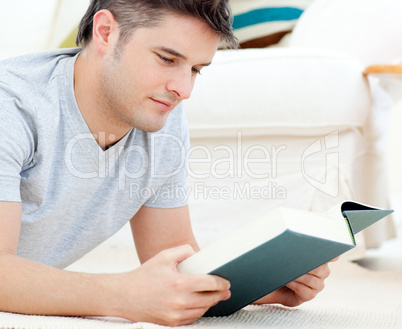 Interested young man reading a book lying on the floor