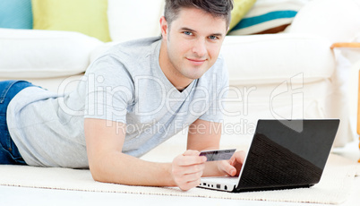Smiling man lying on the floor with laptop holding a card