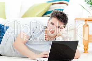 Handsome young man lying on the floor with a laptop