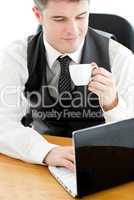 Happy young businessman looking at his laptop holding a coffee