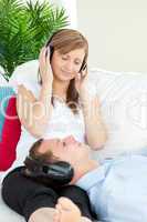 Cute woman listening to music with her boyfriend lying on a sofa