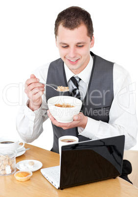 Happy businessman eating cereals looking at his laptop