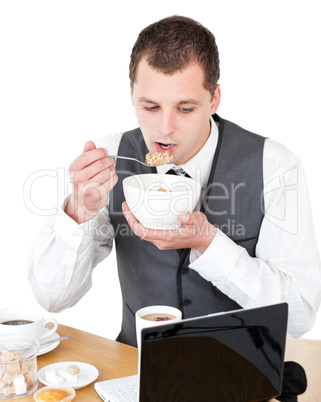 Concentrated businessman eating cereals looking at his laptop