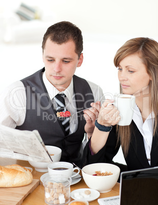 Young couple of business people reading a newspaper while having
