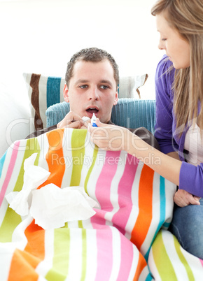 Worried woman examining her boyfriend with a thermometer