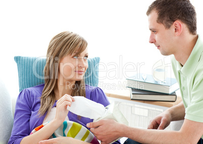 Caring man giving his ill girlfriend tissue lying on a sofa