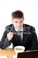 Charming businessman using a laptop while having breakfast