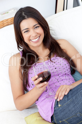 Cute woman sitting on sofa and drinking a glass of red wine