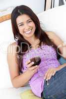 Cute woman sitting on sofa and drinking a glass of red wine