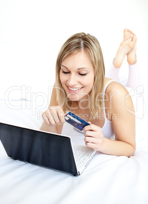 Smiling woman lying with a laptop on sofa