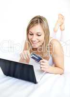 Smiling woman lying with a laptop on sofa