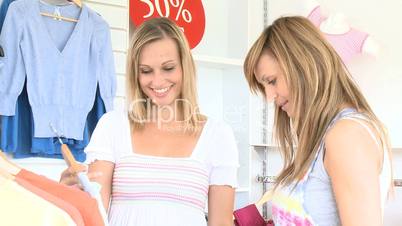 Joyful young woman choosing clothes with her friend in a shop