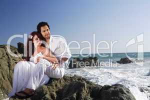 Young couple at the beach sitting on rocks and posing