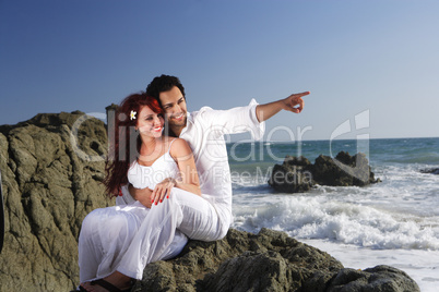 Young couple at the beach sitting on rocks and pointing