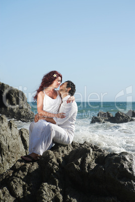 Young couple at the beach sitting on rocks and kissing