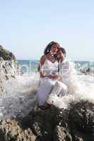 Young couple at the beach sitting on rocks while getting splashed with water