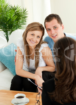Smiling couple listen to a saleswoman siting on a sofa
