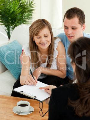Bright young couple signing a contract sitting in their living r
