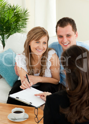 Happy young couple signing a contract sitting in the living room