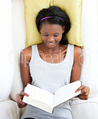 Bright female teenager reading a book lying on a sofa