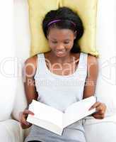 Bright female teenager reading a book lying on a sofa