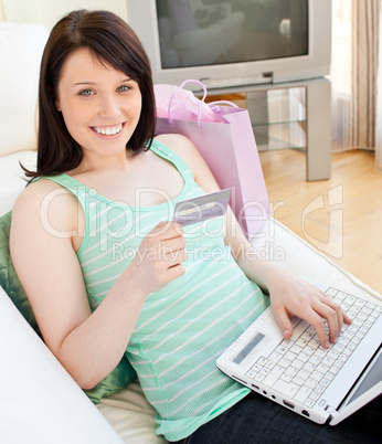 Glowing young woman holdign a card using her laptop