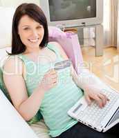 Glowing young woman holdign a card using her laptop