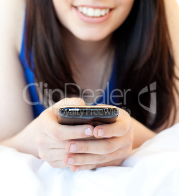 Close-up of a brunette teenager texting while lying on her bed