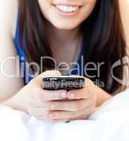 Close-up of a brunette teenager texting while lying on her bed
