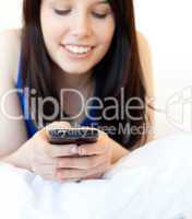 Radiant young woman texting while lying on a bed