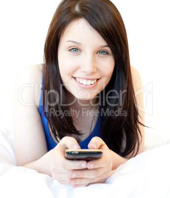 Happy young woman texting while lying on a bed