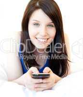 Happy young woman texting while lying on a bed