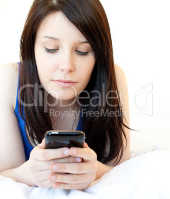 Concentrated young woman texting while lying on a bed