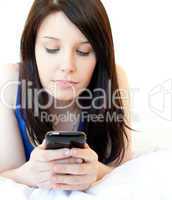 Concentrated young woman texting while lying on a bed