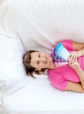 Cheerful woman lying on a sofa holding color sample