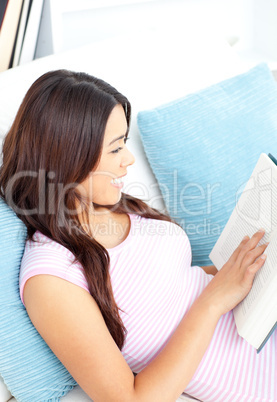 Delighted woman sitting on her sofa reading a book