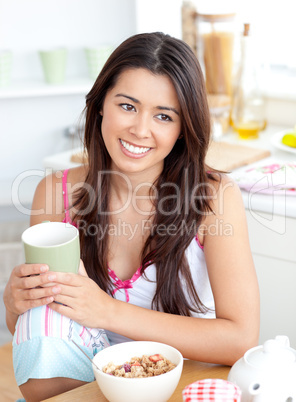 Radiant asian woman holding a cup sitting at breakfast table