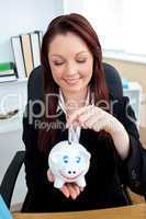 Cute businesswoman putting money in a  piggybank