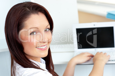 Charming businesswoman using her laptop smiling at the camera