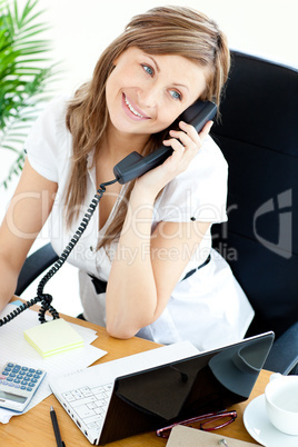 Bright businesswoman talking on phone sitting in her office
