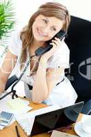 Bright businesswoman talking on phone sitting in her office