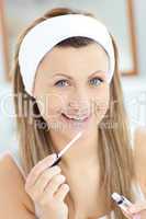 Delighted woman applying gloss on her lips