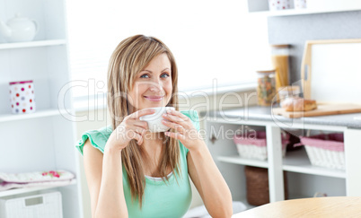 Cute young woman drinking coffee sitting in the kitchen