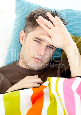 Sick young man feeling his temperature lying on the sofa