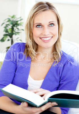 Bright caucasian woman reading a book sitting on a sofa