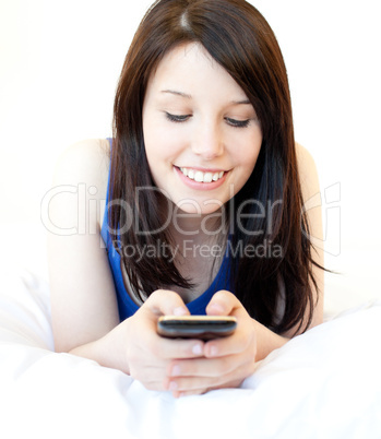 Happy female teenager using cellphone lying on the bed