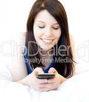 Happy female teenager using cellphone lying on the bed
